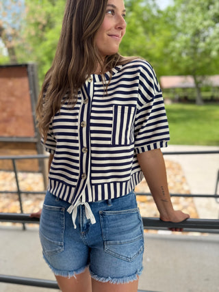 Woman wearing a striped shirt and denim shorts standing outdoors.
