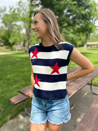 Woman wearing a sleeveless sweater with red star patterns in a park setting