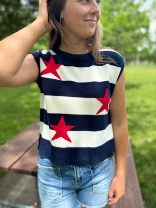 Woman wearing a sleeveless sweater with red star patterns outdoors.
