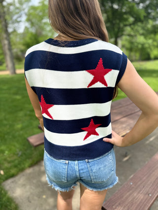 Person wearing a sleeveless sweater with red star patterns outdoors.