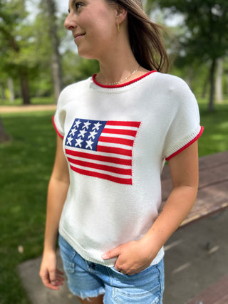 Woman wearing a white sweater with an American flag design outdoors.