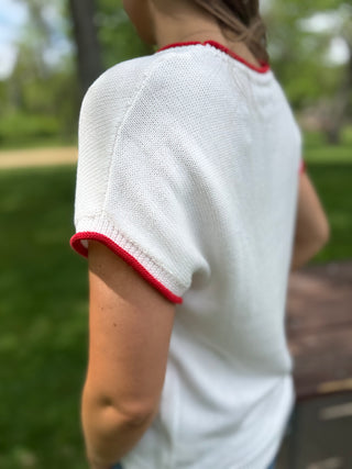 Person wearing a white shirt with red trim in an outdoor setting