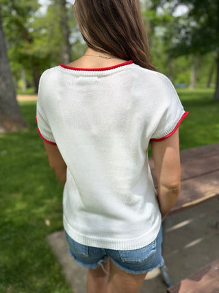 Person wearing a white sweater with red trim in a park setting