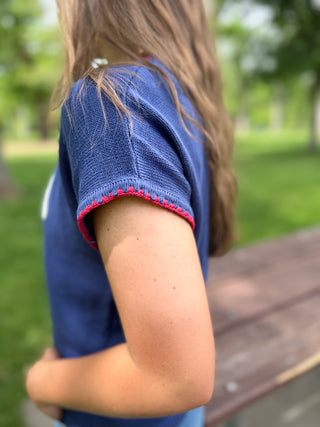 Person wearing a blue shirt with red trim in an outdoor setting