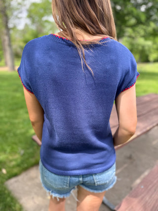 Person wearing a blue sleeveless top with red trim outdoors