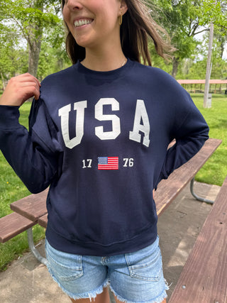 Person wearing a navy blue sweatshirt with 'USA' and an American flag design, standing outdoors.
