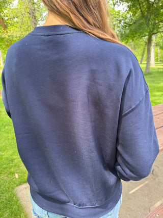 Person wearing a navy blue sweatshirt outdoors with green grass and trees in the background