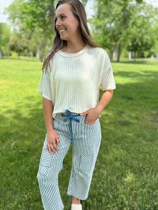 Woman standing in a park wearing a light-colored top and striped pants.