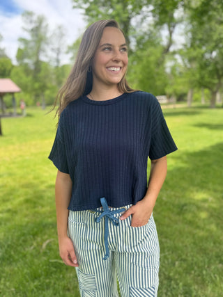 Woman wearing a navy blue shirt and striped pants standing in a park.