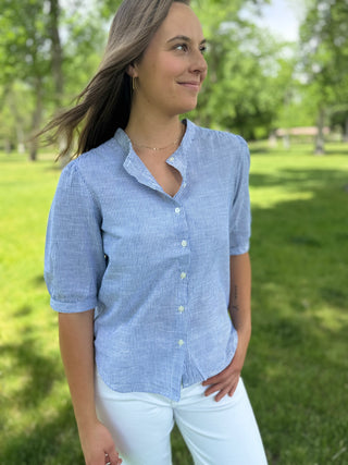 Woman wearing a blue checkered shirt and white pants standing in a park.