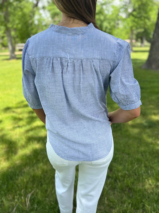 Person wearing a blue checkered shirt and white pants standing in a grassy area.