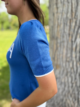 Person wearing a blue sweater with white trim standing next to a tree