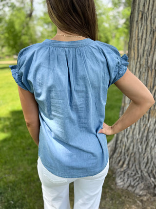 Person wearing a blue top and white pants standing outdoors near a tree