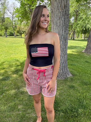 Woman wearing a strapless top with an American flag design and red and white striped shorts in a park.
