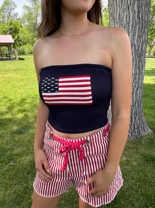 Person wearing a bandeau top with an American flag design and matching shorts in a park setting.