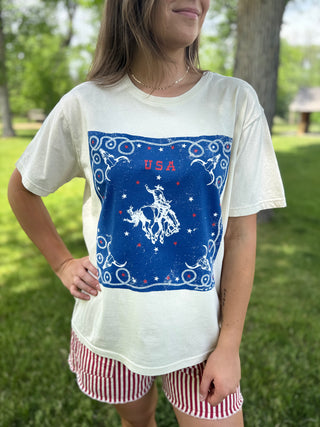 Person wearing a white t-shirt with a blue graphic design outdoors.