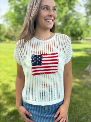 Woman wearing a white mesh top with an American flag design outdoors.