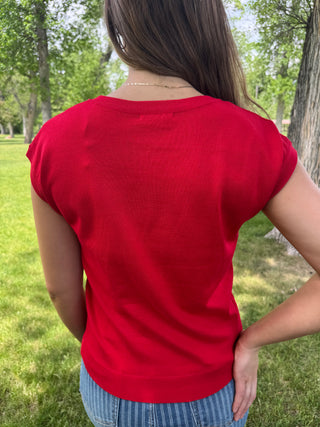 Person wearing a red shirt and blue jeans standing in a park.