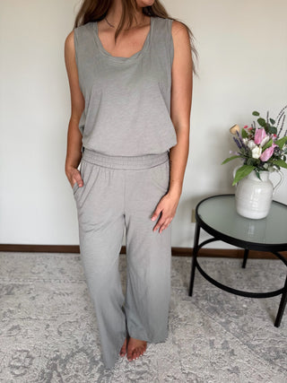 Person wearing a gray sleeveless top and pants in a minimal indoor setting.