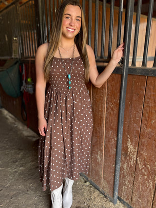 Woman in a brown dress standing next to a wooden stable door.