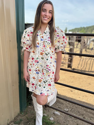 Woman wearing a floral dress standing near a fence with a rural background