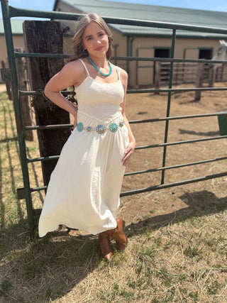 Woman in a white dress standing next to a metal gate in an outdoor setting with buildings in the background.
