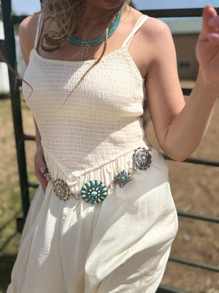 Person wearing a white dress with a decorative belt featuring turquoise and silver designs.