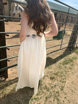 Person in a white dress standing near a metal fence with a horse in the background