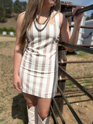 Woman in a striped dress and boots standing next to a metal gate outdoors.