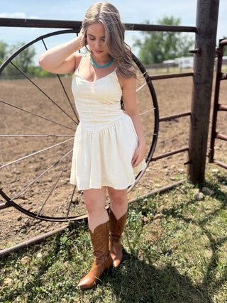Woman in a white dress and brown boots standing in front of a rustic metal gate.