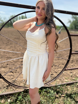 Woman in a white dress standing in front of a large metal wheel in an outdoor setting