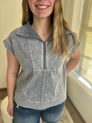 Lady wearing a charcoal grey half zip cap sleeve top.
