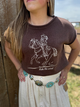 Person wearing a brown shirt with a horse and rider design, standing outdoors.