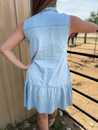 Person wearing a light blue denim dress standing near a fence with a blurred background