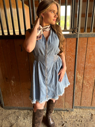 Woman in a denim dress and knee-high boots standing in a stable.