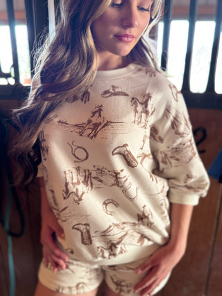Woman wearing a cream-colored t-shirt with brown graphic designs in an indoor setting.