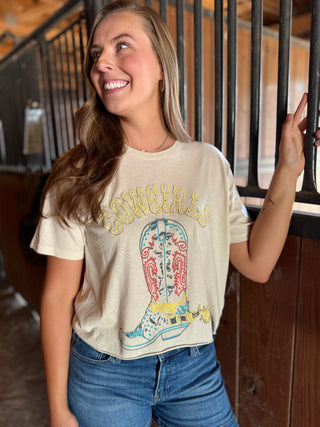 Woman wearing a t-shirt with a cowboy boot graphic and 'Cowgirl' text, standing in a rustic setting.