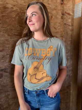 Woman wearing a t-shirt with 'Cowboy Country' graphic design against a wooden background