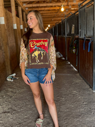 Woman wearing a graphic t-shirt with a horse and cowboy design in a barn setting.