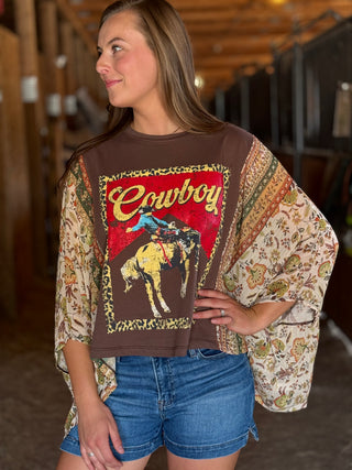 Woman wearing a patterned shirt with a 'Cowboy' graphic in a rustic setting