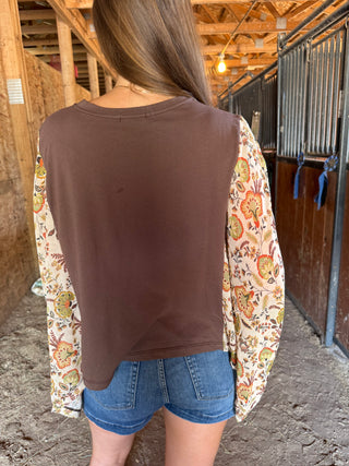 Person wearing a brown vest over a floral shirt with denim shorts in an indoor setting.