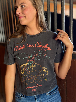 Woman wearing a t-shirt with 'Ride 'em Cowboys' graphic design in an indoor setting.