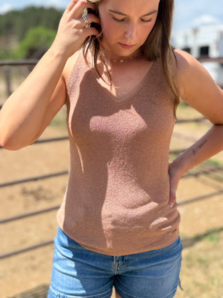 Woman wearing a sparkly brown tank top and blue jeans outdoors.