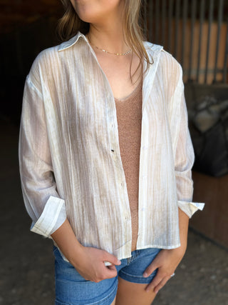 Woman wearing a sheer beige striped shirt over a brown top and blue shorts.