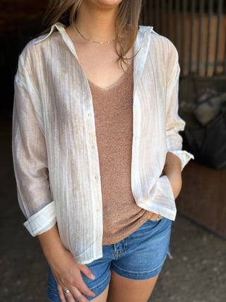 Woman wearing a sheer white blouse over a brown top and blue shorts in an outdoor setting.