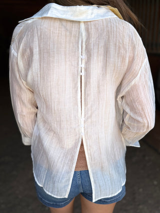 Back view of a person wearing a sheer beige blouse with a dark background
