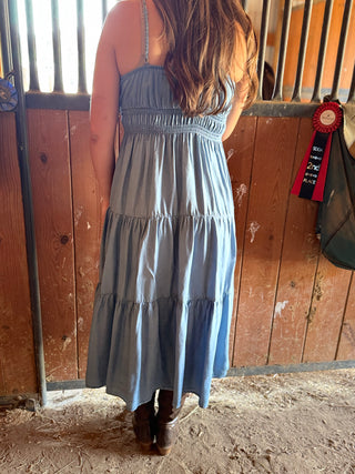 Person wearing a blue dress standing in a stable with a wooden fence and a ribbon on the wall.