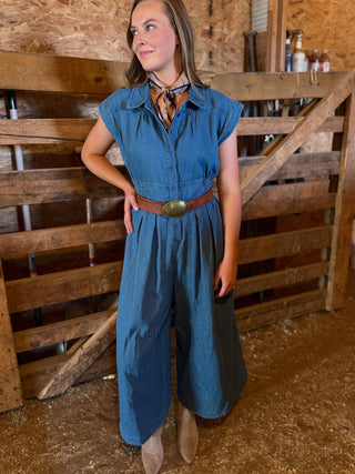 Woman wearing a blue jumpsuit standing in front of wooden pallets.