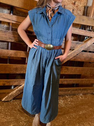 Woman wearing a denim dress with a belt in front of wooden pallets.