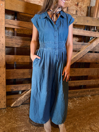 Woman wearing a blue denim dress standing in front of wooden pallets.
